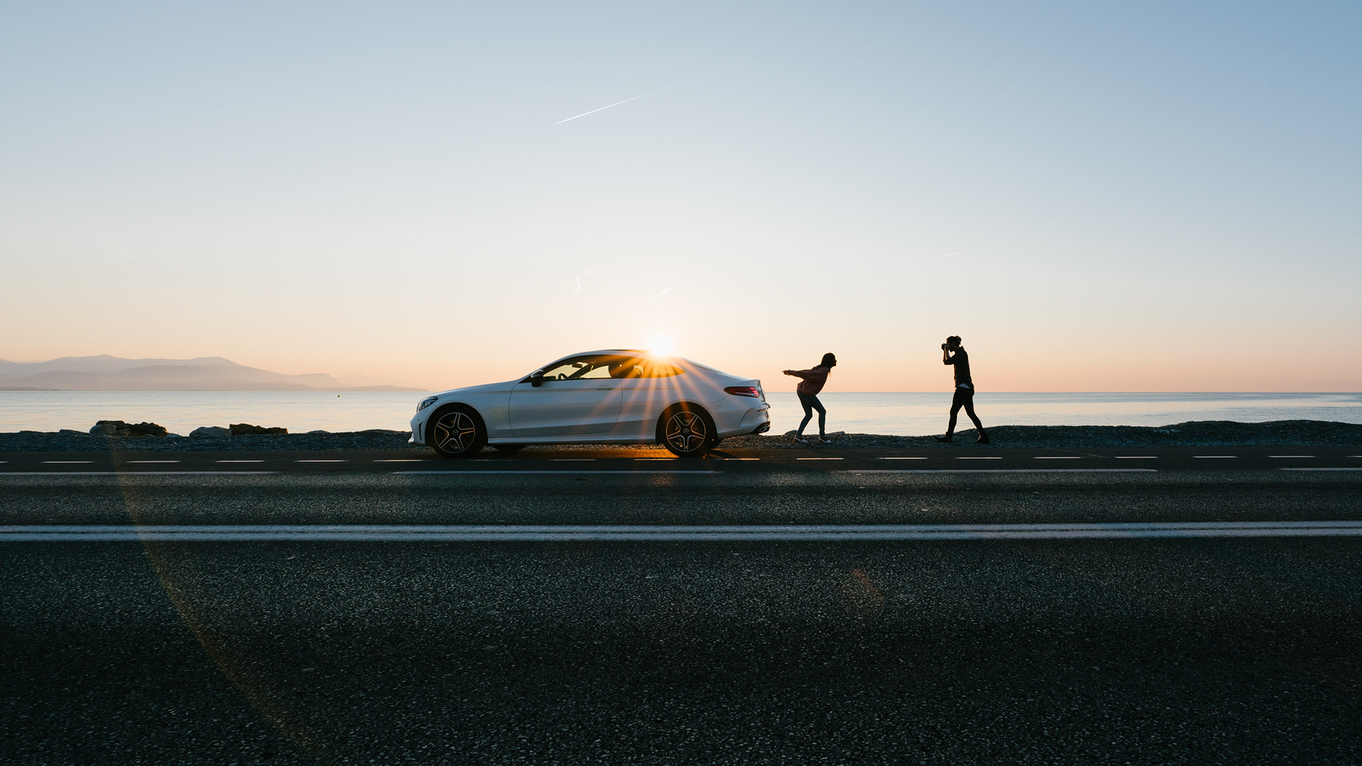 Auto auringonlaskussa ja maisemassa kaksi ihmistä mukana