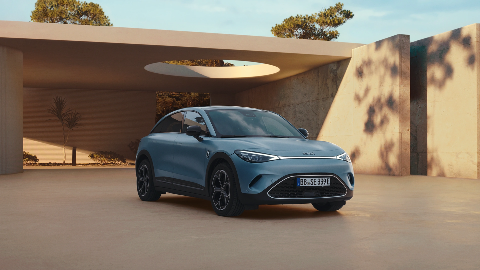 Sininen smart #3 henkilöauto kuvattuna ilta-auringossa tyylikkään autokatoksen edessä.