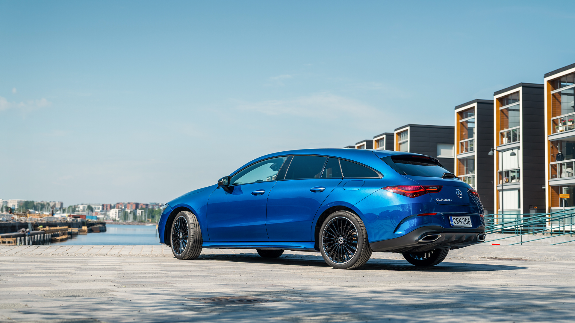 Sininen CLA henkilöauto meren rannalla urbaanissa ympäristössä.
