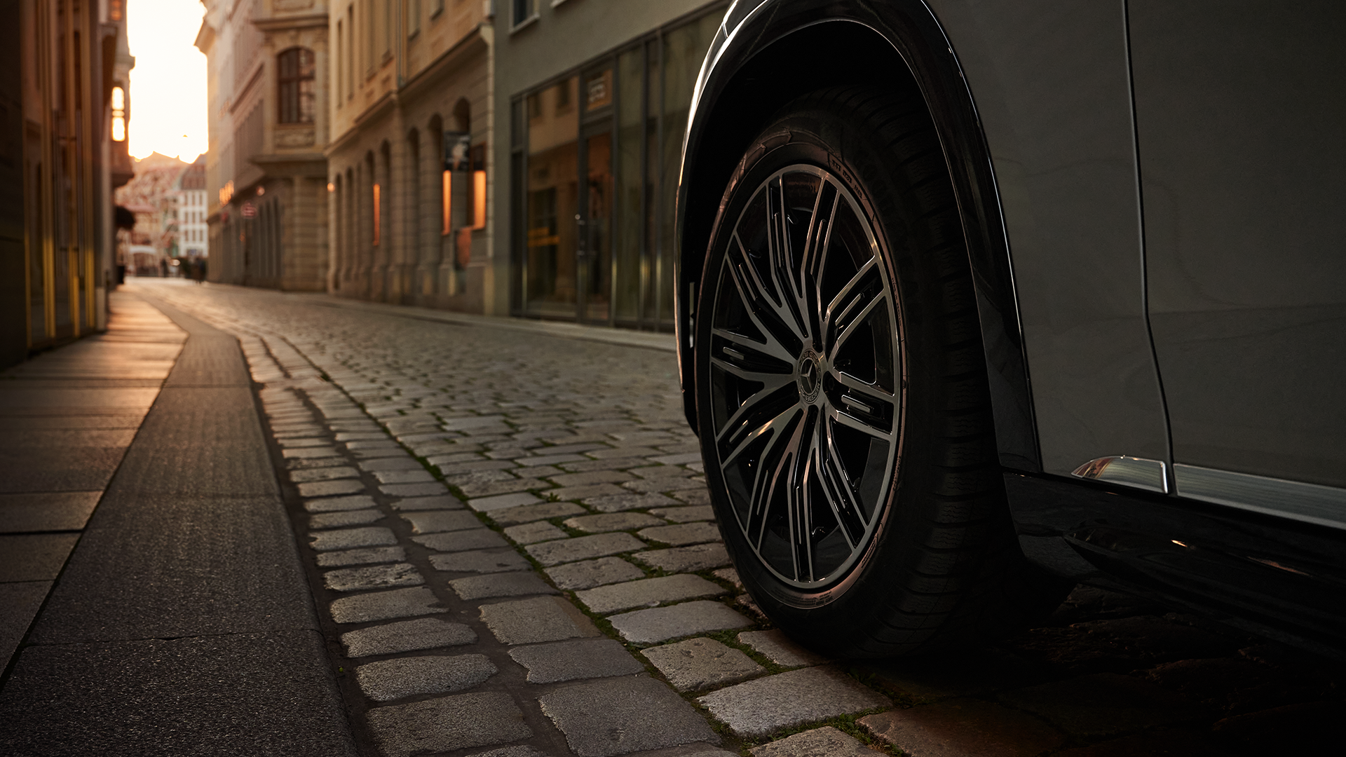 Mercedes-Benz ajamassa kaupungin kapeaa mukulakivikatua. Talojen välistä tien päässä pilkistää aurinko.