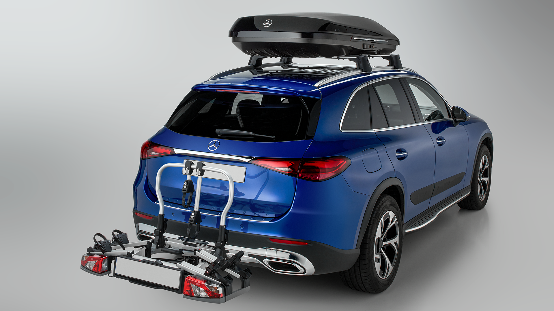 Sähkönsininen Mercedes-Benz SUV, joka varusteltu suksiboksilla sekä vetokoukkuun asennettavalla polkupyörätelineellä.