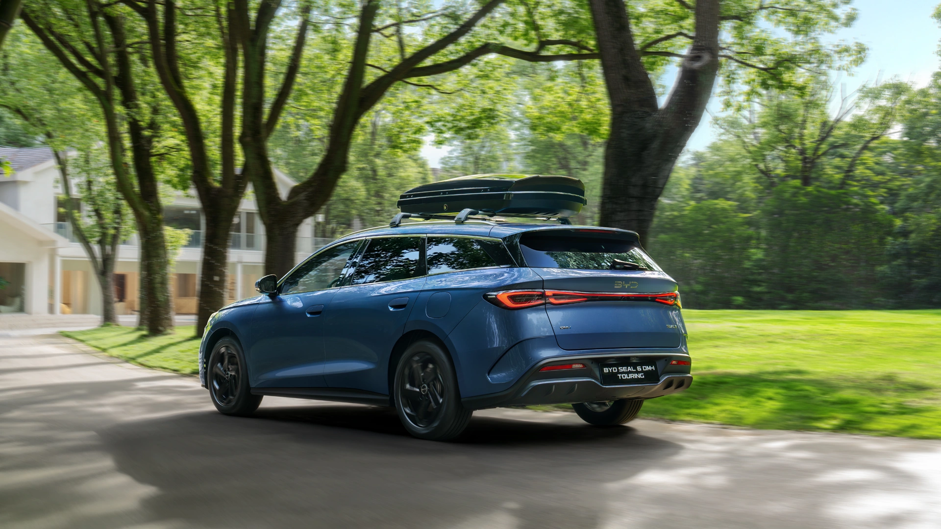 Perheauto BYD Seal 6 DM-i farmari puistomaisemassa. Kattokiskoilla suksiboksi.