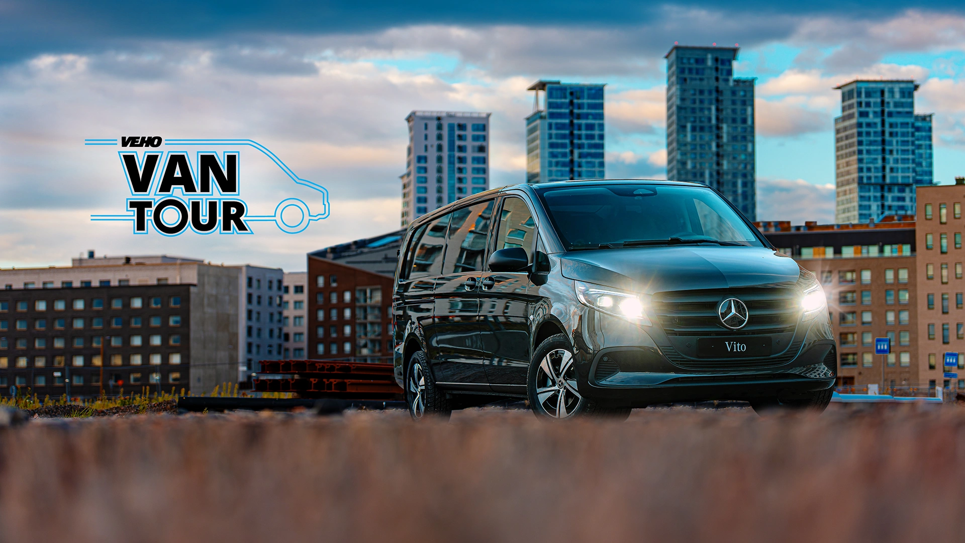 Veho Van Tour -logo ja Mercedes-Benz Vito kerrostalojen edessä