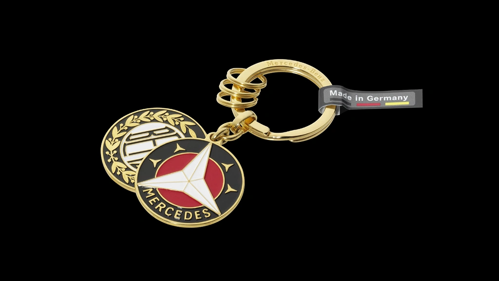 Kullattu avaimenperä yhdistää näyttävän ulkonäön ja käytännöllisen rakenteen. Litteään avainrenkaaseen laserkaiverrettu Mercedes-Benz-teksti sekä yksipuoliset riipukset 1909 Benz- ja 1916 Mercedes -logoilla.