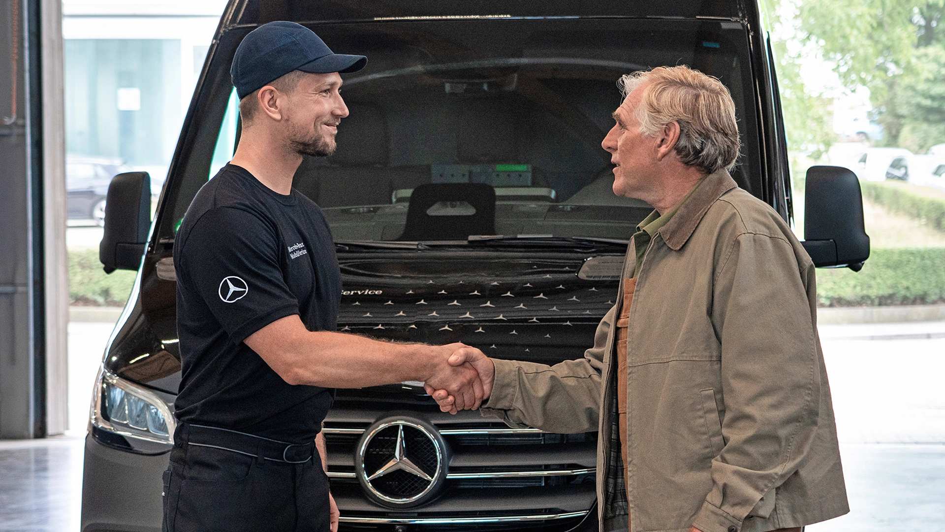 Kaksi miestä kättelee Mercedes-Benz Sprinterin keulan edessä.