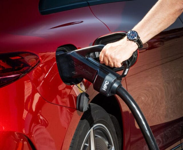 Lähikuva auton latauksesta: henkilön käsi asettamassa latauspistoketta