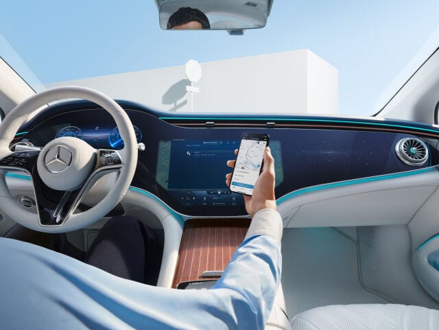Auton sisätila, kuskilla kädessä puhelin, jonka näytöllä näkyy Mercedes sovellus avattuna