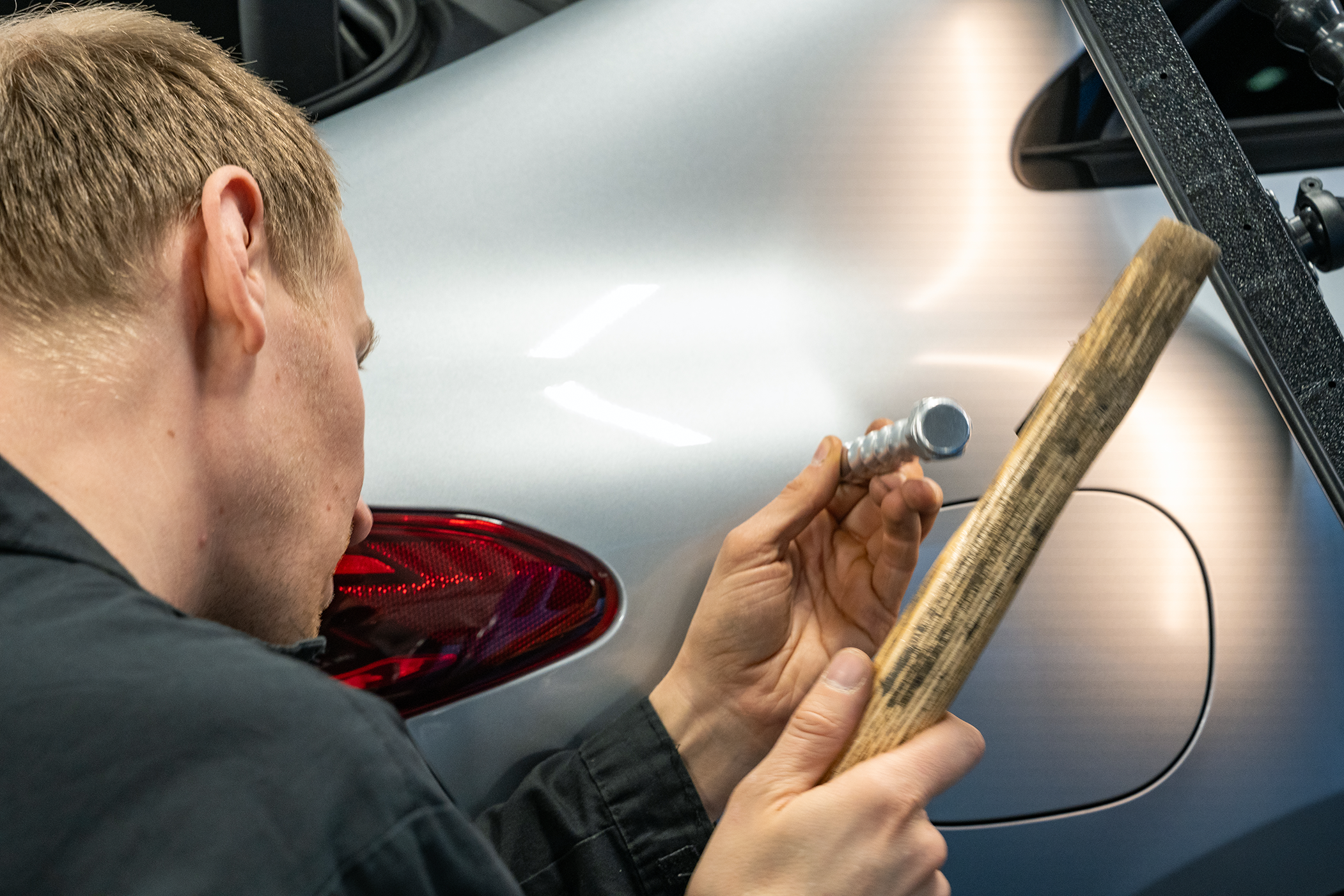 Vehon mekaanikko suorittamassa pdr-korjausta (paintless dent removal) auton takalokasuojalle.