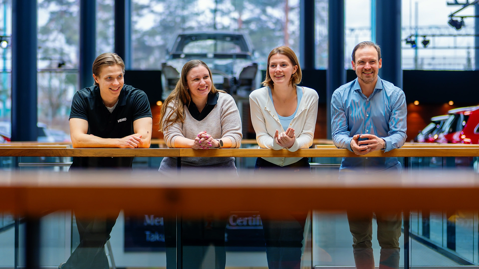 Kaksi miestä ja kaksi naista seisoo kaiteen edessä Veho Aiport autoliikkeessä ja hymyilee