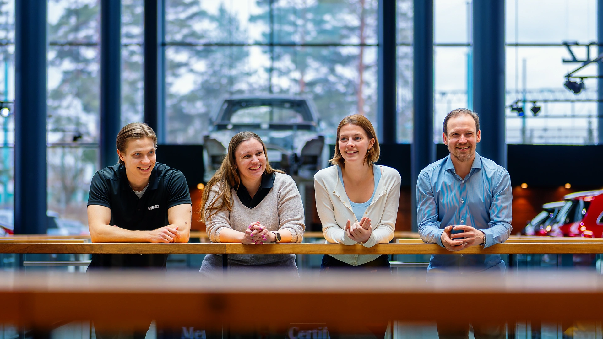 Kaksi hymyilevää naista ja kaksi miestä seisoo kaiteen edessä Veho Aiport autoliikkeessä ja hymyilee
